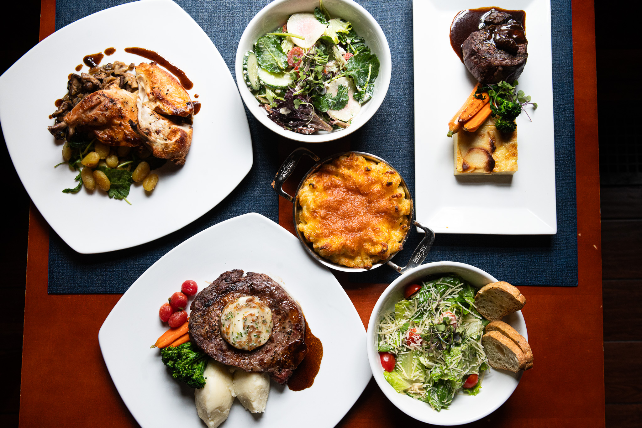 overhead shot of various food including steak, baked chicken, mac & cheese, and salad